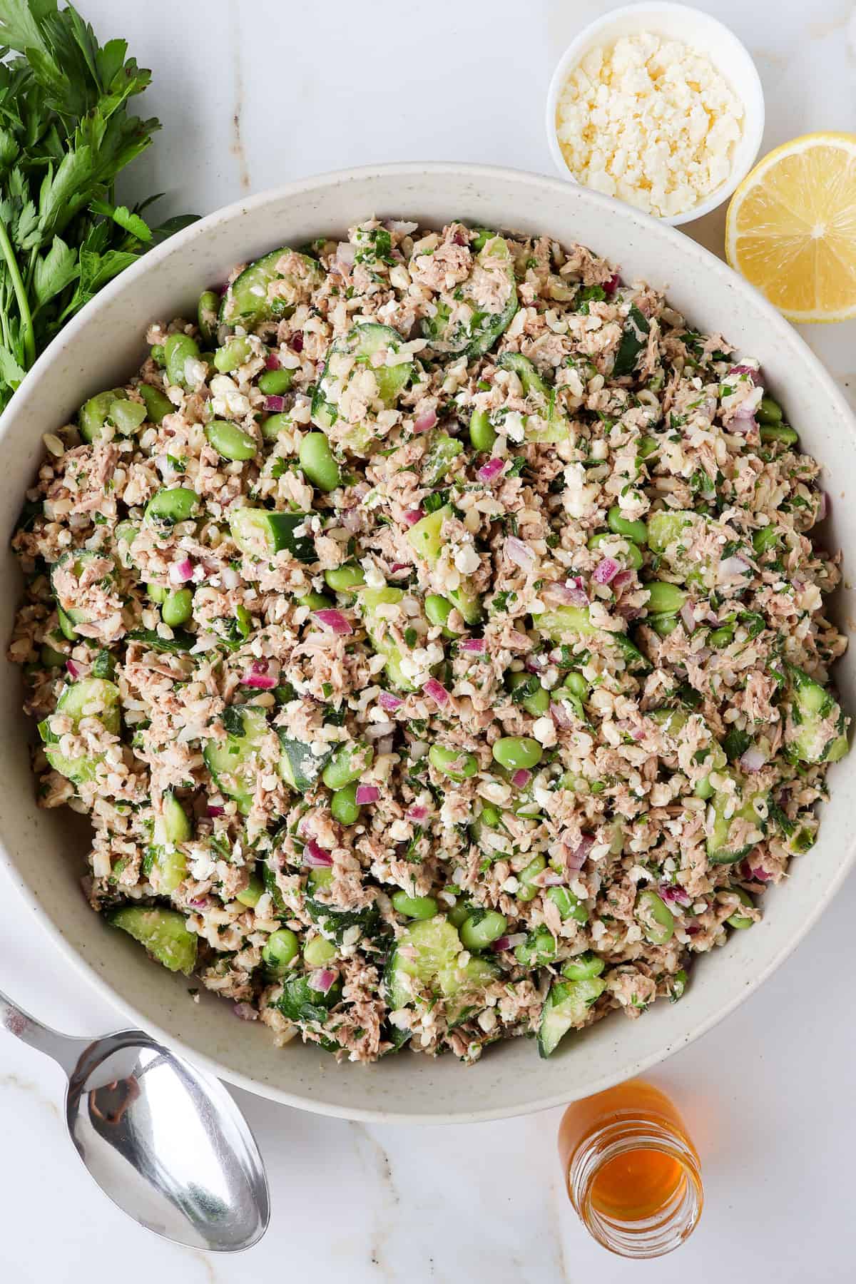 Tuna cucumber salad in a bowl with parsley, feta, lemon and honey in a jar on the sides.