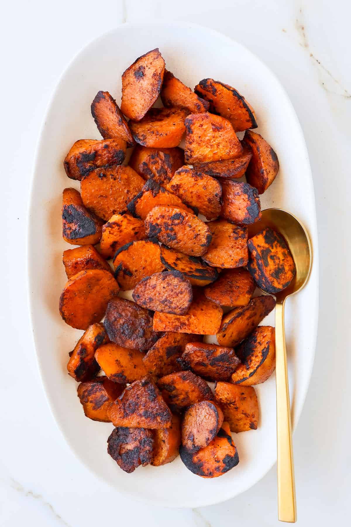 Sautéed sweet potato served on a platter with a gold spoon.