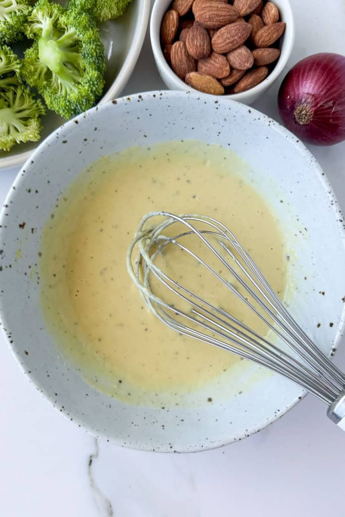 Tahini mustard dressing in a bowl with a whisk.