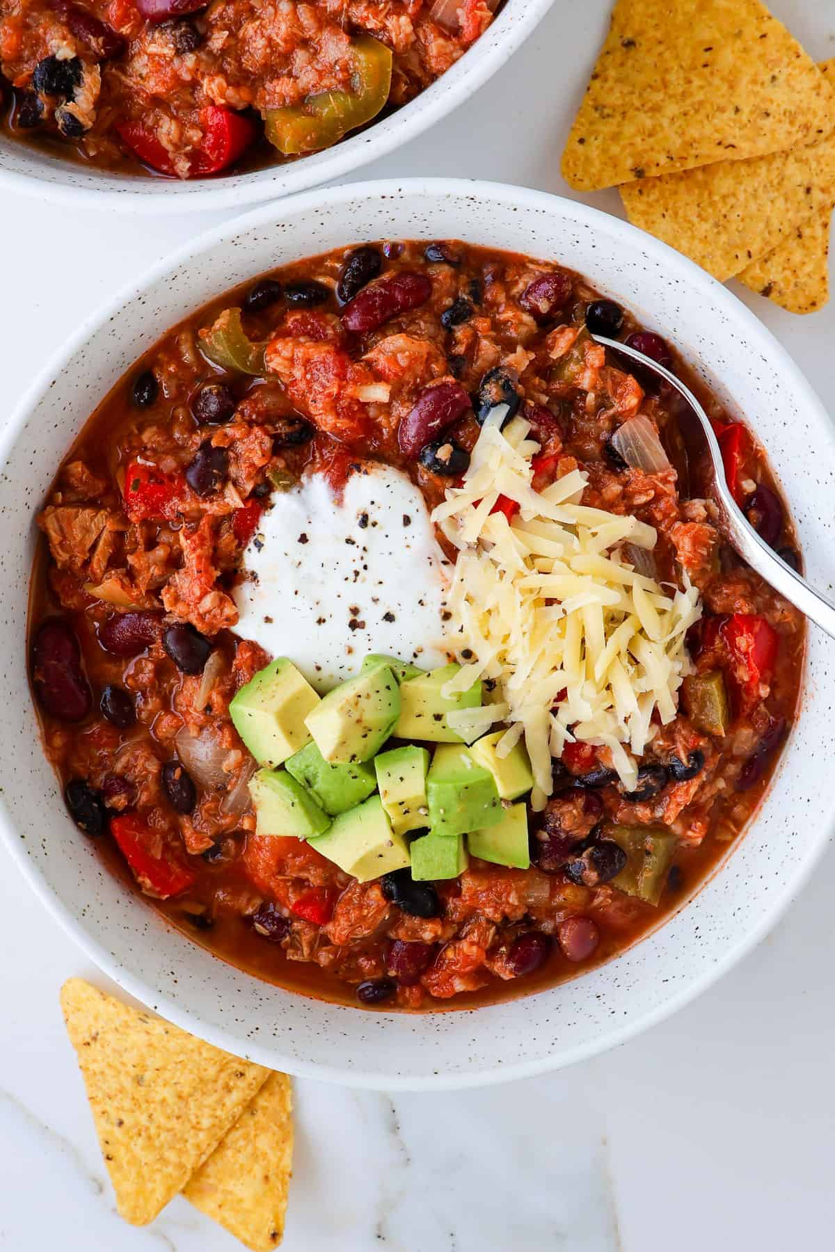 Chili in a bowl with avocado cubes, cheese and yogurt on top.