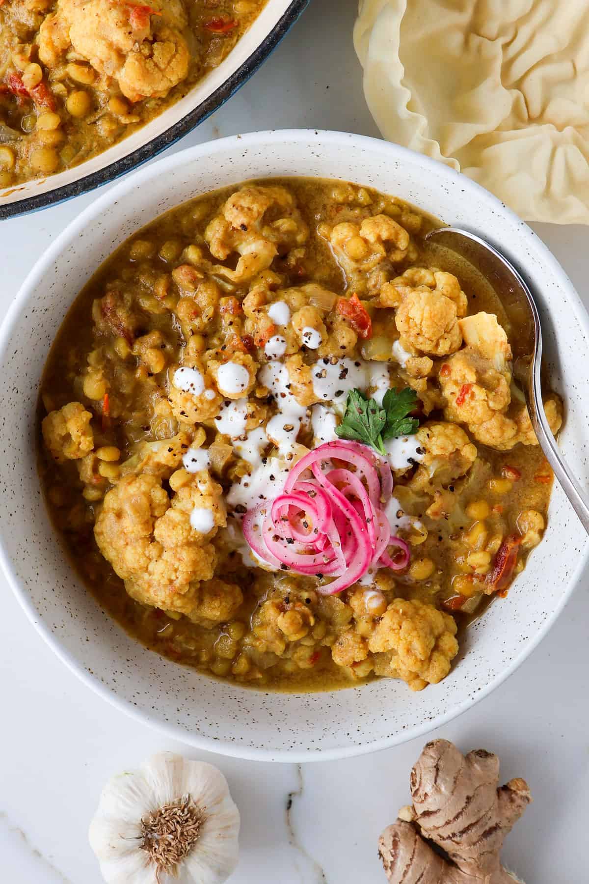Split pea curry in a bowl with yogurt and pickled onions on top.